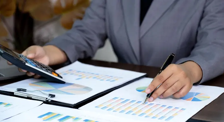 Persoon analyseert financiële grafieken op papier met een rekenmachine.